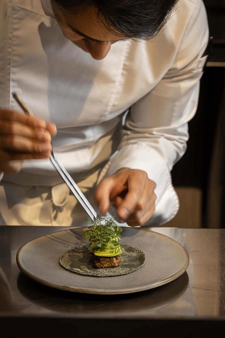 The chef finishing a dish with fresh herbs