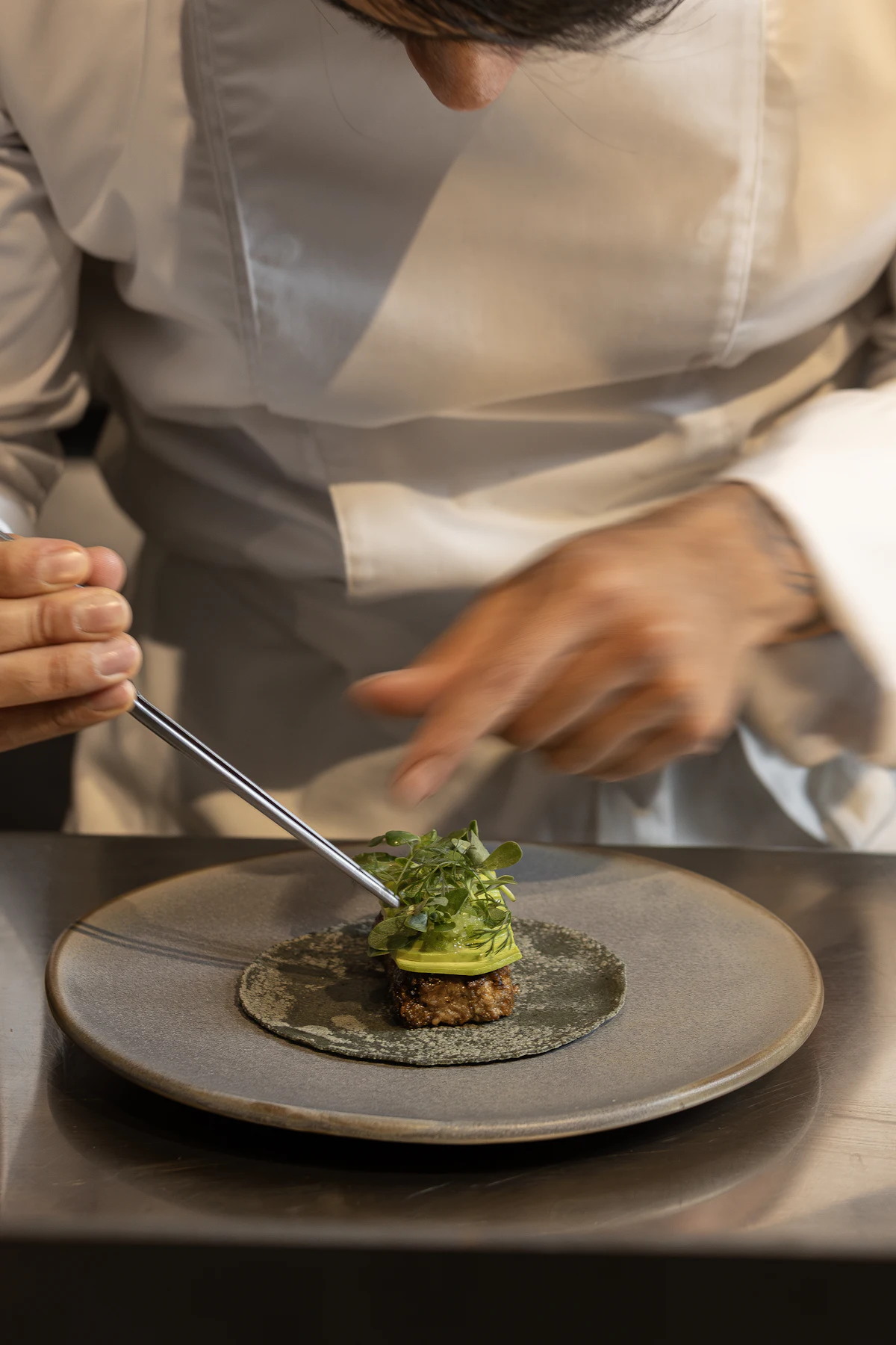 The head chef plating a dish with tweezers